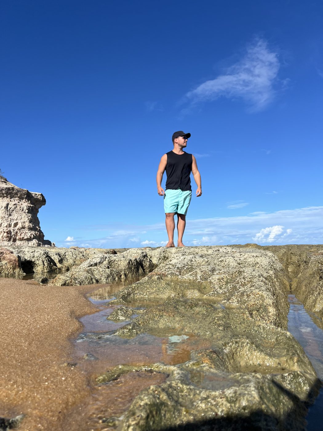Matheus Colombo em pé sobre as pedras da praia